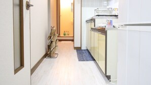 A narrow hallway with a wooden floor leading to a kitchen area with white cabinets and a blue mat. - Furere Shichijo (Kyoto)