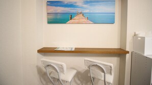 A room with a wooden shelf, two white chairs, and a painting of a pier leading to a calm sea. - Furere Shichijo (Kyoto)