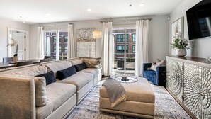Una sala de estar moderna con un sofá beige, un sillón azul, una mesa de centro y un aparador decorativo.