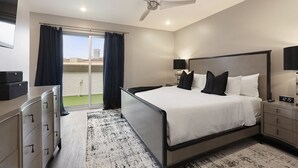 Habitación de hotel moderna con una cama grande, un escritorio, una silla, un ventilador de techo y vistas de la ciudad a través de la ventana.