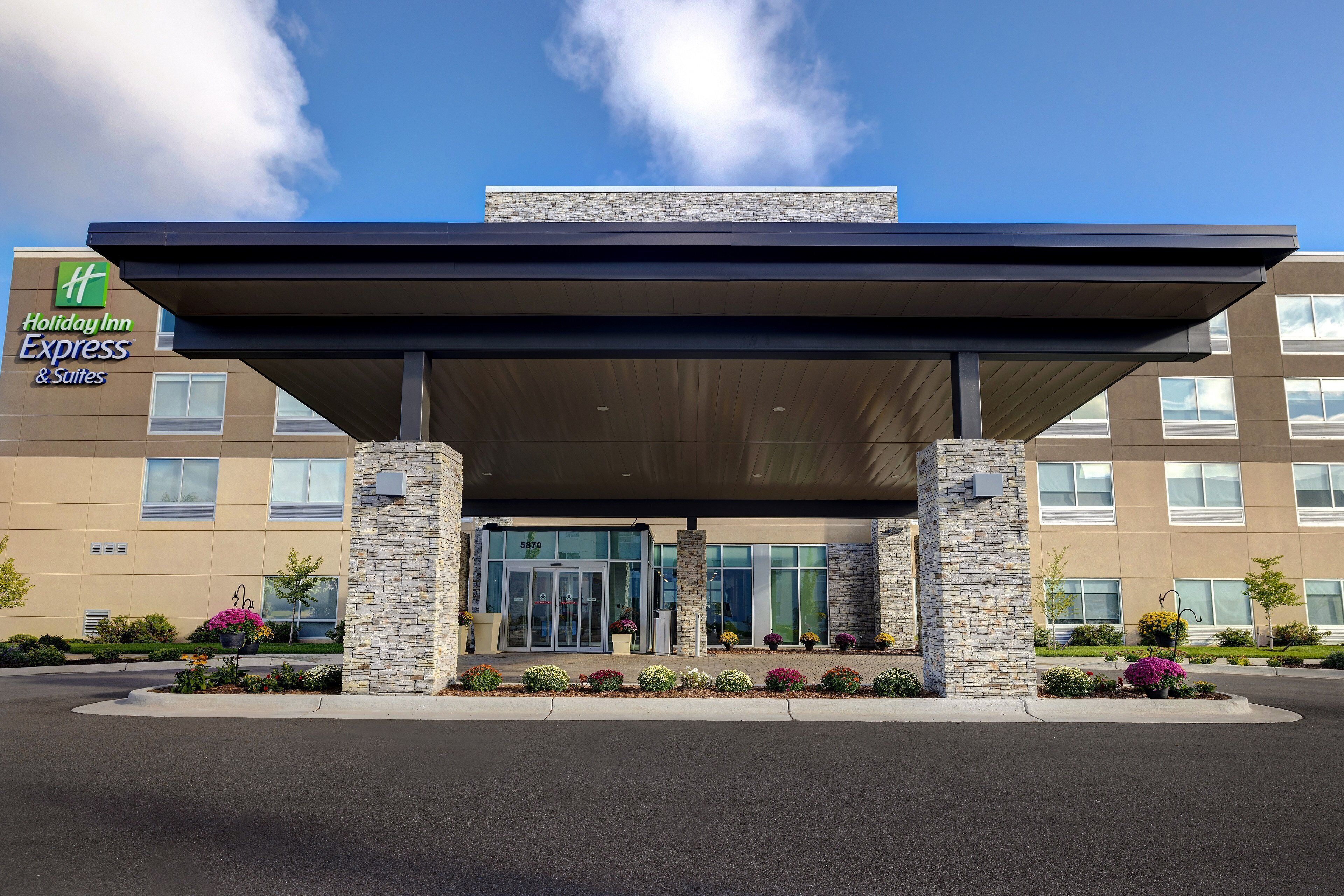 A Holiday Inn Express & Suites building with a covered entrance, stone pillars, and a landscaped front with various plants.