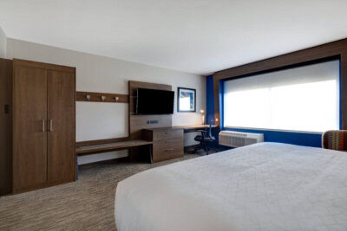 Une chambre d’hôtel avec un grand lit, un bureau avec une chaise, une télévision et une armoire.
