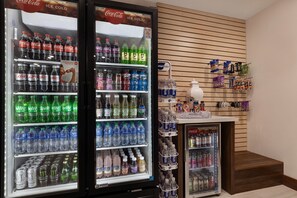 Un área de venta automática con refrigeradores de Coca-Cola y Sprite, un dispensador de agua y una exhibición de snacks.