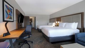 Habitación de hotel con escritorio, dos camas, una silla y televisor.