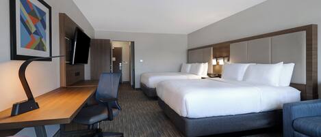 A hotel room with a desk, two beds, a chair, and a TV.