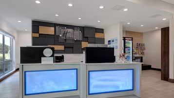 En hotellobby med modern design, med en receptionsdisk med upplysta paneler, en digital skärm och en väggmonterad skylt med hotellets namn.