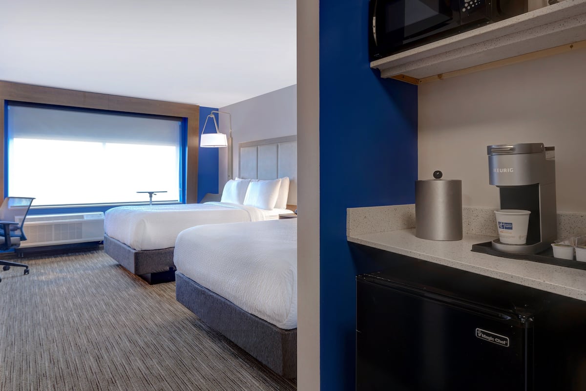 Une chambre d’hôtel avec deux lits, un bureau, une chaise, un four à micro-ondes, une machine à café et un réfrigérateur.
