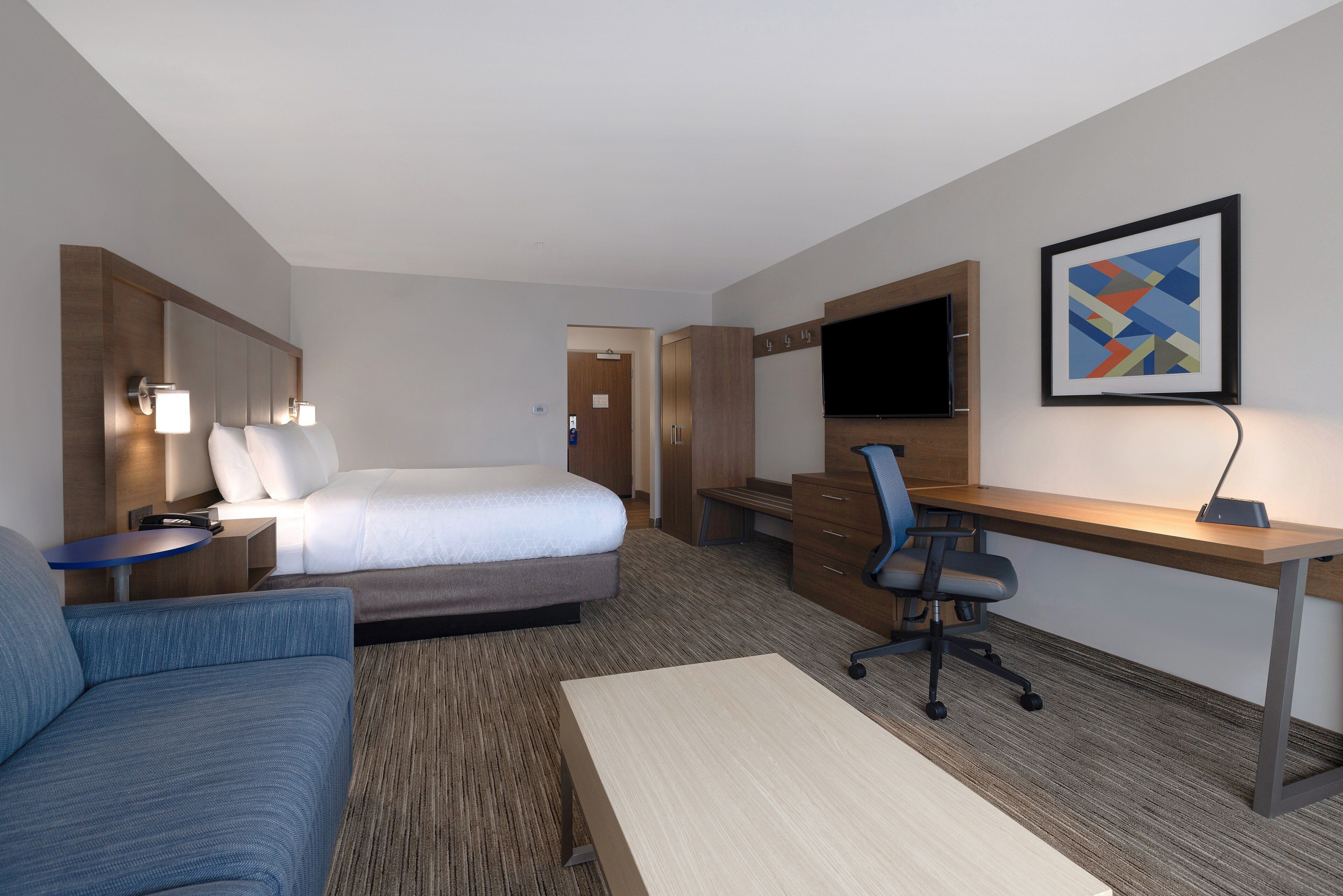 A hotel room with a bed, a desk, a chair, a television, and a framed picture on the wall.