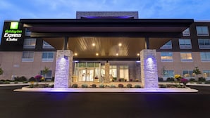 Un bâtiment Holiday Inn Express & Suites doté d’une entrée couverte, de piliers en pierre et d’un parterre fleuri aménagé à l’avant.