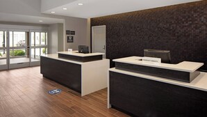 Ein Hotel-Empfangsbereich mit modernem Design, mit zwei Empfangstresen, einer Wand mit Muster und einer Tür zum Außenbereich.