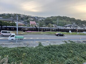 A train passing by a road with vehicles and a green car. - Oyado Midokoi (Akune)