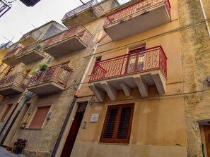 A multi-story building with balconies, some with red railings and others with decorative metalwork.