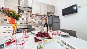 A modern kitchen with a dining table set for two, featuring a bottle of wine, a bowl of cherries, and decorative glassware. - Vacation home SinAgo by Interhome (Lascari)