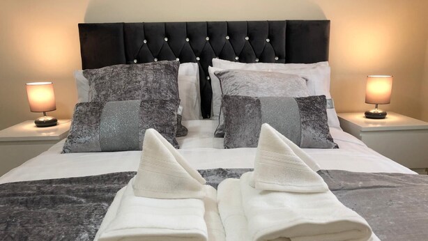 A neatly made bed with a black headboard, two pillows, and two folded towels. - Green Apartments (Manchester)
