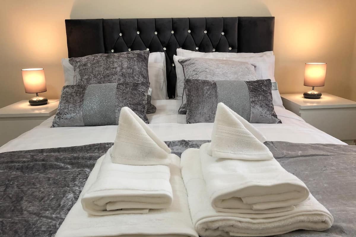 A neatly made bed with a black headboard, two pillows, and two folded towels.