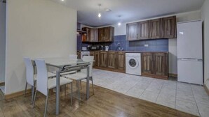 A modern kitchen with wooden cabinets, a built-in washing machine, and a dining area with a table and chairs. - Green Apartments (Manchester)