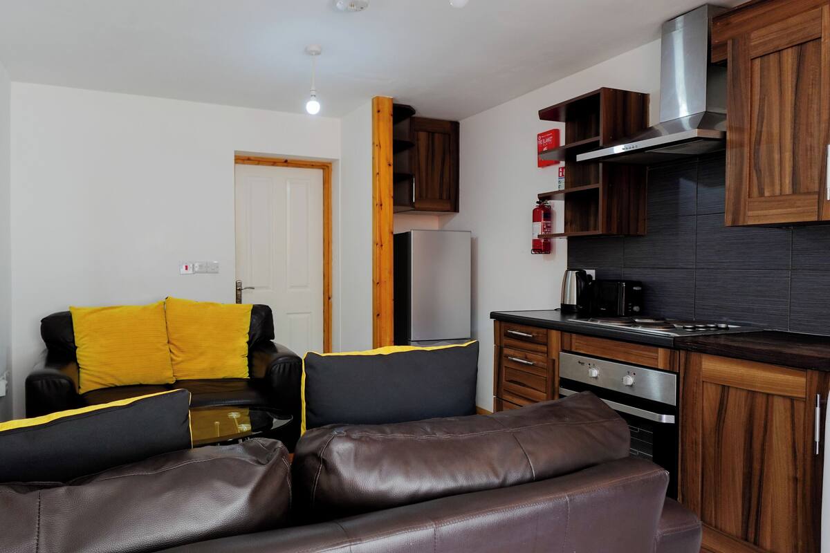 A compact living space with a sofa, a small kitchen area, and a door leading to another room.