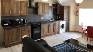 A modern kitchen with wooden cabinets, a black stove, a washing machine, and a dining area with a red chair. - Green Apartments (Manchester)