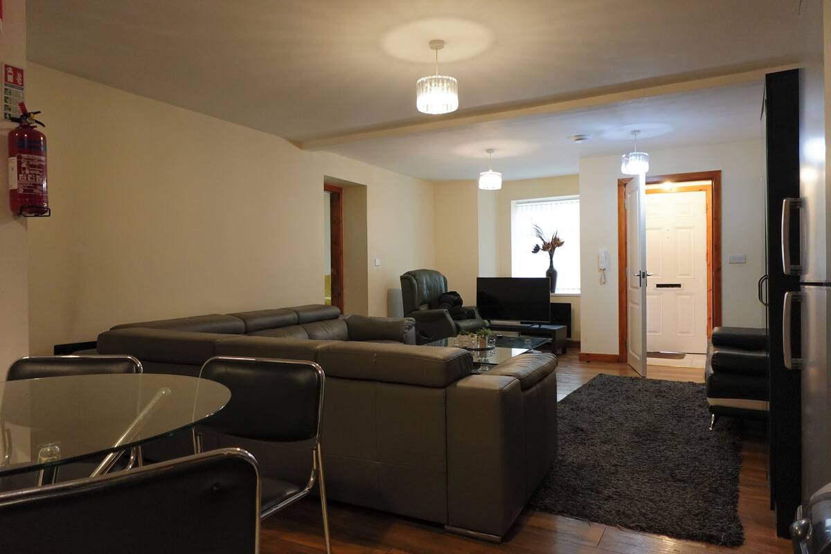A modern living room with a sectional sofa, a glass dining table, and a black leather chair.