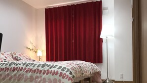A bedroom with a bed, a red curtain, a floor lamp, and a wall-mounted light fixture.