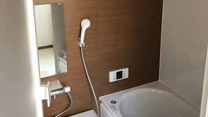 A bathroom with a bathtub, a toilet, a mirror, and a wall-mounted light fixture.