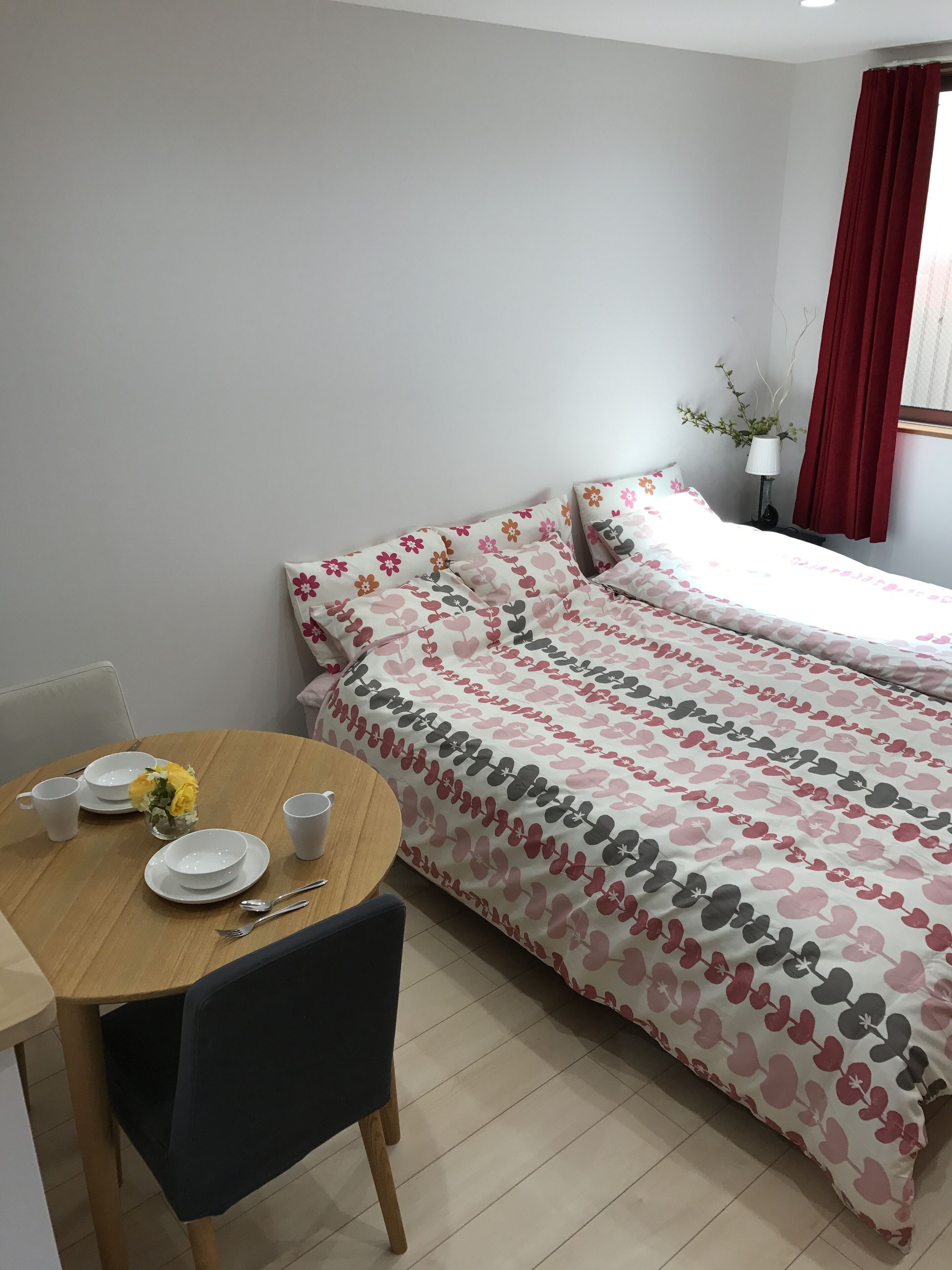 A bedroom with a bed, a bedside table, a chair, and a small table with a vase of flowers.