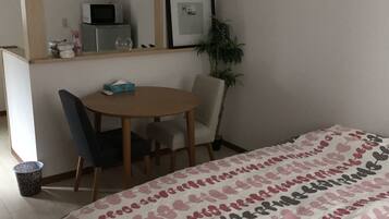 A bedroom with a bed, a desk, a chair, a microwave, a framed picture, and a potted plant.