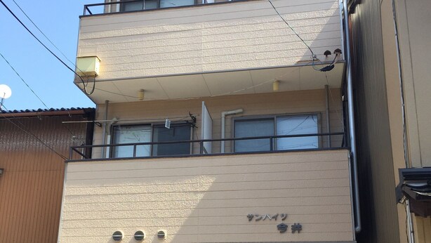 Un edificio de varios pisos con entrada a nivel de calle, una señal visible y un balcón en el segundo piso.