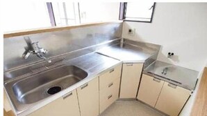 Cocina compacta con pileta de acero inoxidable, una pequeña mesada y muebles color beige.