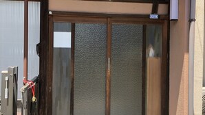 A building entrance with a glass door, a metal gate, and a concrete step leading up to the door. - Kanazawa-Hachitabi Hashiba (Kanazawa)