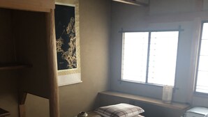 A traditional Japanese room with tatami flooring, a low wooden bed with pillows, a small table with a vase, and a window with a view. - Kanazawa-Hachitabi Hashiba (Kanazawa)