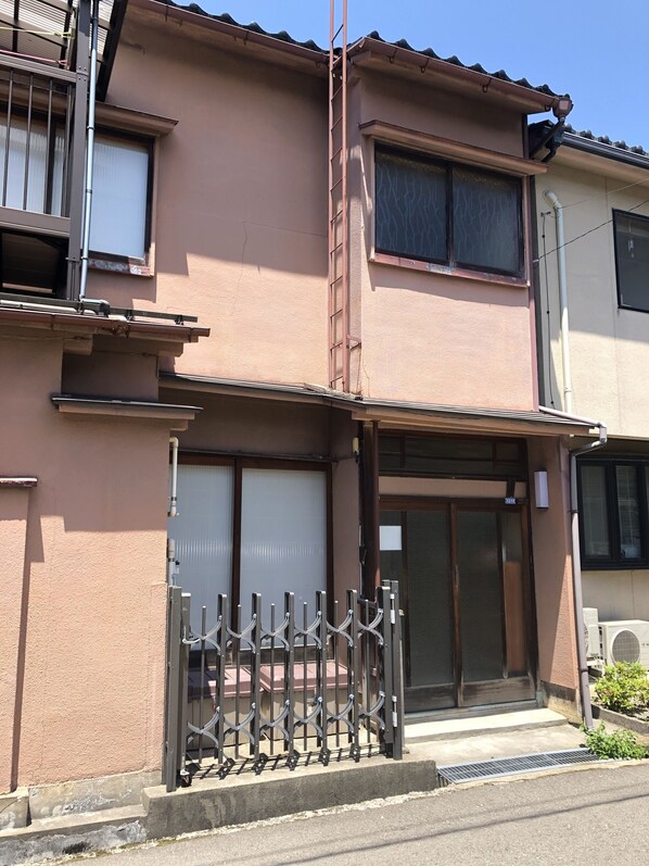 Un edificio residencial de dos pisos con una reja metálica, un pequeño porche y el número 1218 visible en la puerta.