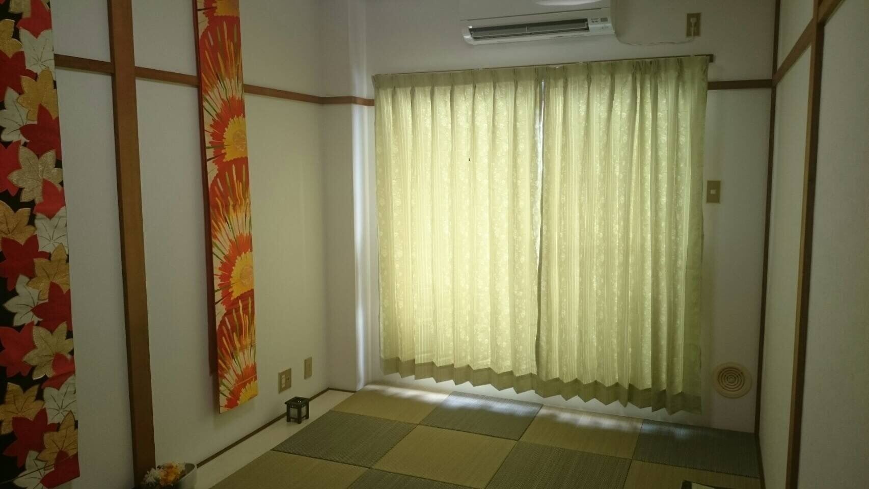 A room with tatami flooring, a shoji screen, and a large window with sheer curtains.