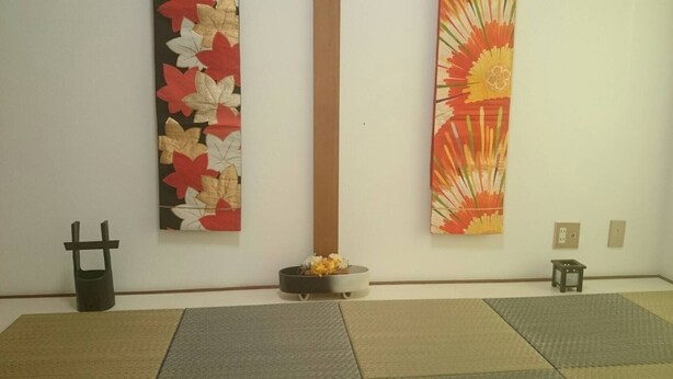 Une pièce dont un long mur est orné de deux grandes peintures florales, avec une petite table sur laquelle est posé un vase de fleurs et une sculpture noire.