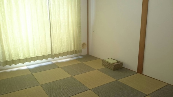 Une pièce avec un sol recouvert de tatamis, un paravent de type shoji et une petite boîte de rangement.