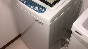 A front-loading washing machine with a control panel, a basket of folded clothes, and a hose connected to the machine. - Kanazawa-Hachitabi Konjiki (Kanazawa)