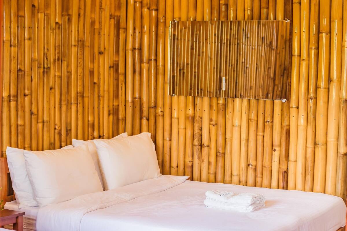 Una habitación con dos camas, piso de madera y pared de bambú.