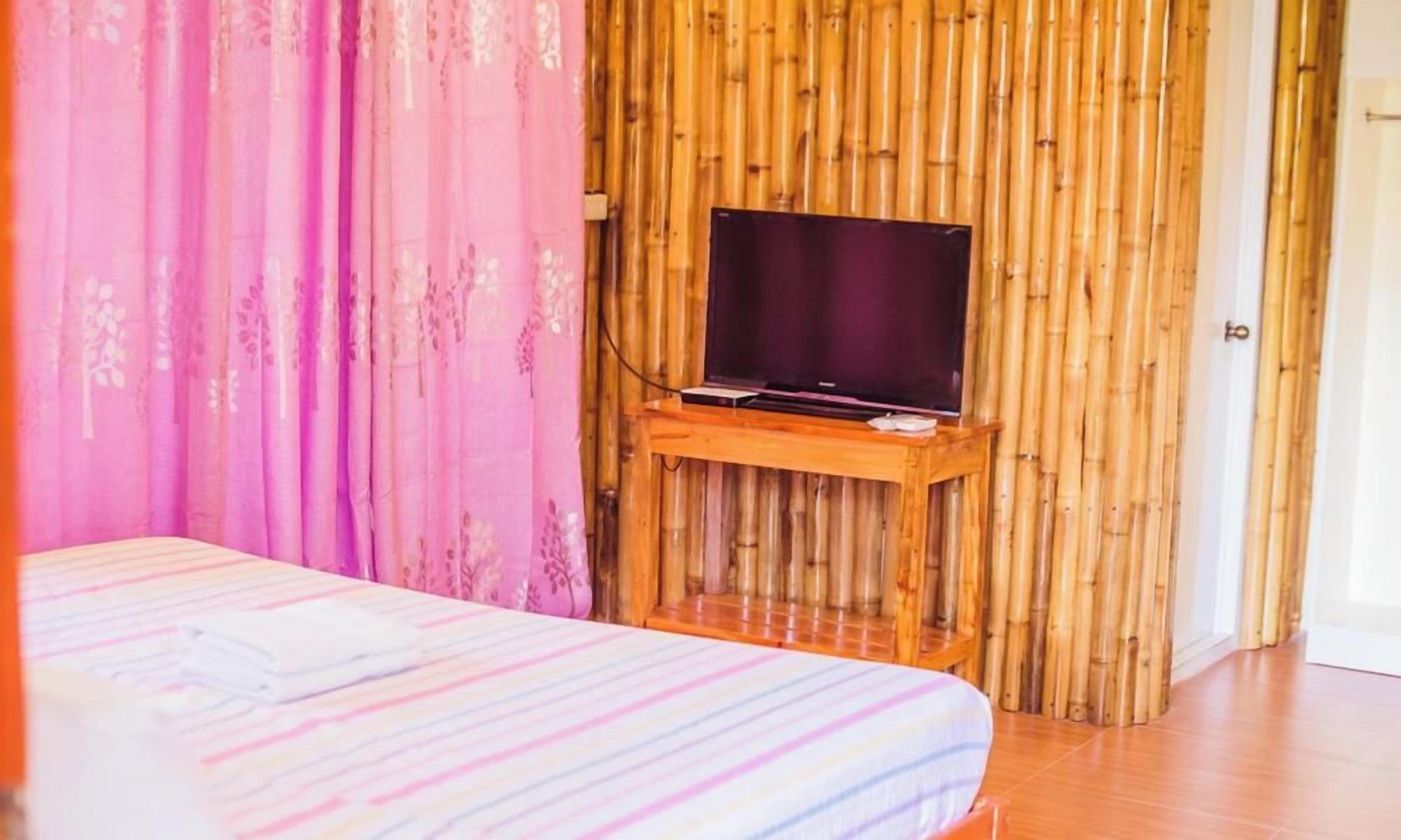 A room with a bed, a television on a wooden stand, and a bamboo wall.