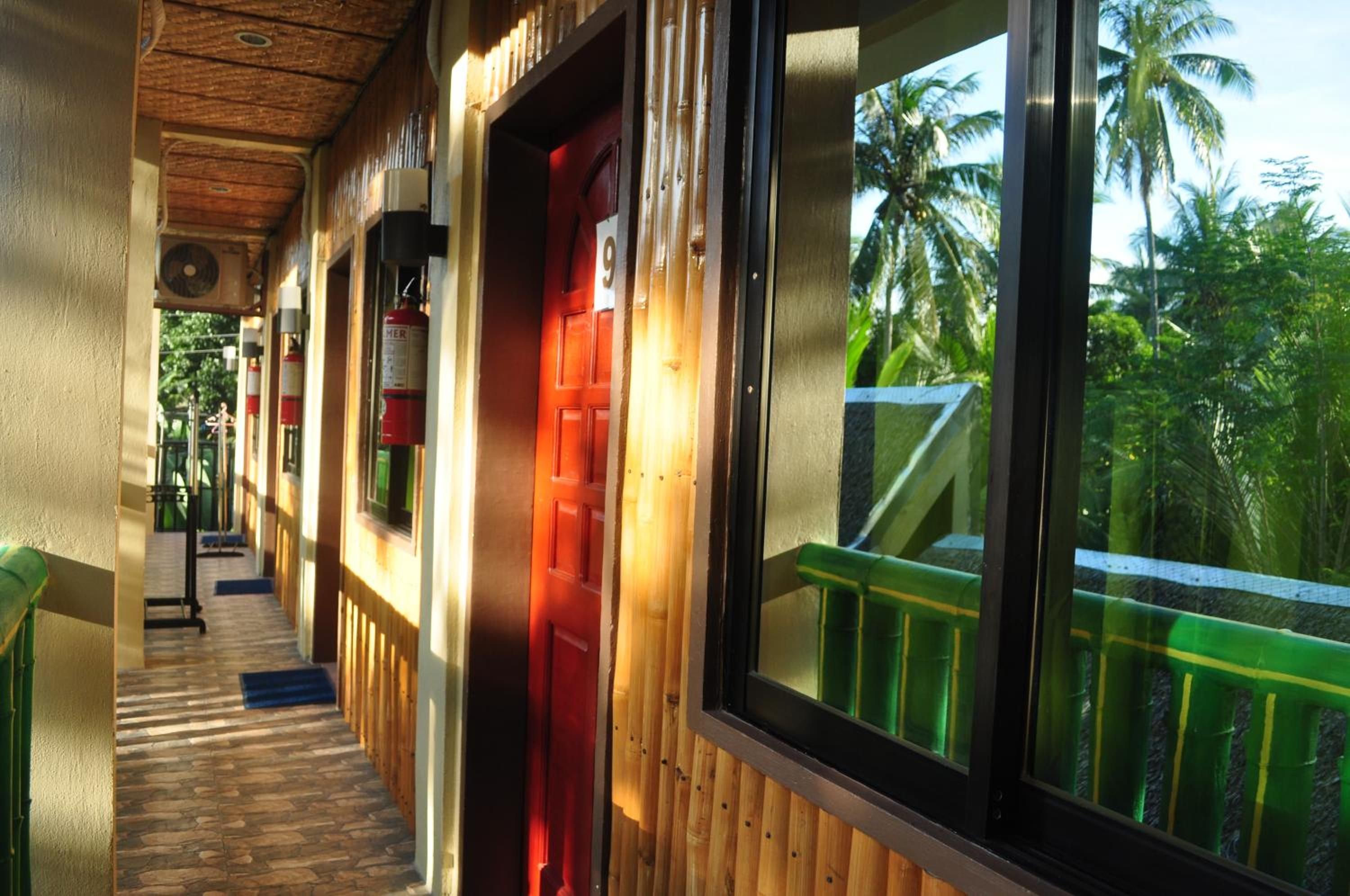 A corridor with a wooden floor, a red door, and a window with a view of palm trees.