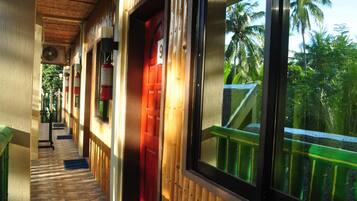 A corridor with a wooden floor, a red door, and a window with a view of palm trees.
