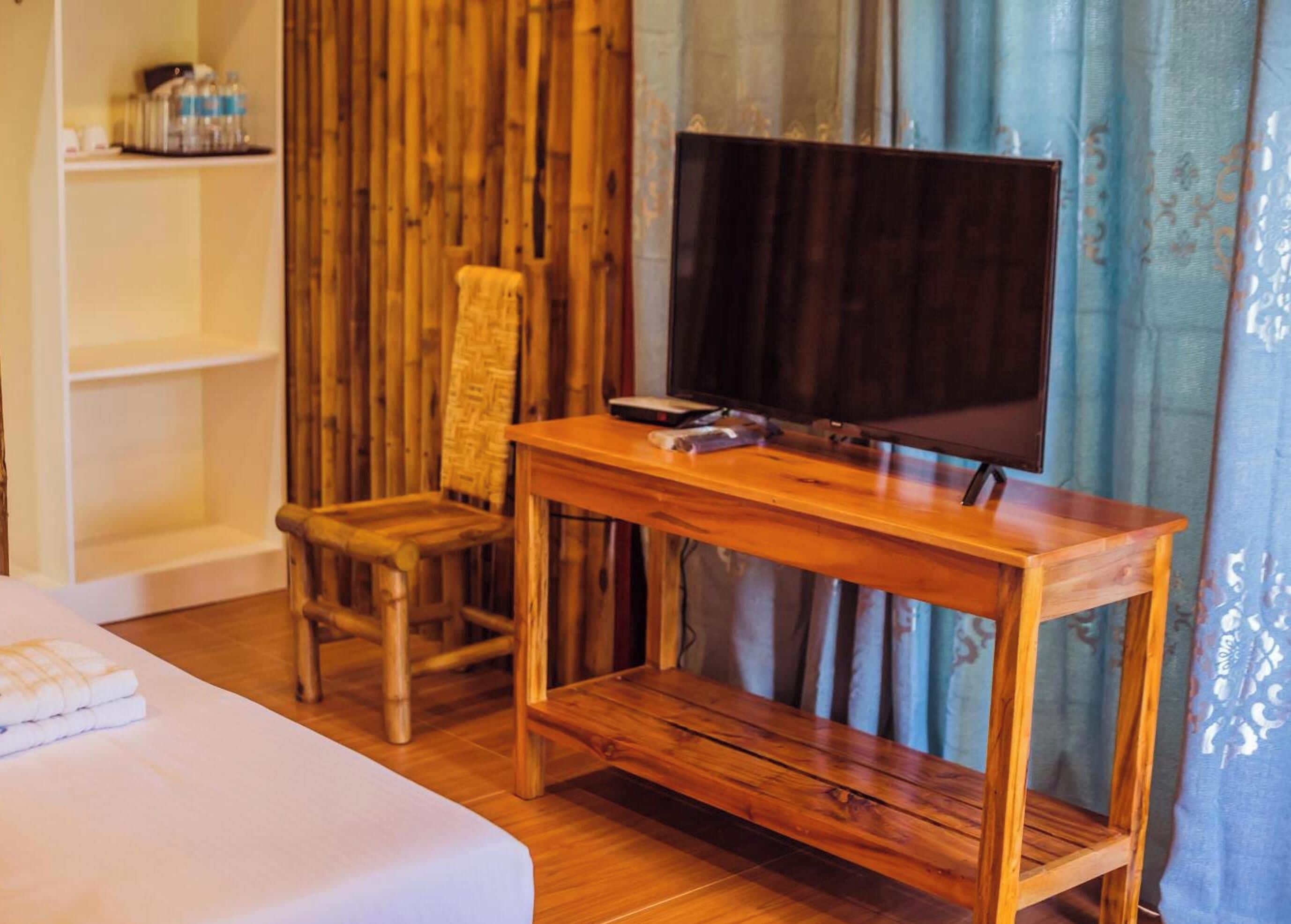 Una habitación con una cama, una silla de madera, un televisor sobre un mueble de madera y una repisa con objetos.