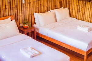 Habitación con dos camas, cada una con ropa blanca y almohadas, una mesita con una planta y un muro de bambú.
