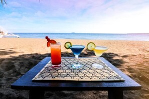 A table with three drinks on a patterned mat at a beach. - Ceazar's Place (Dauin)