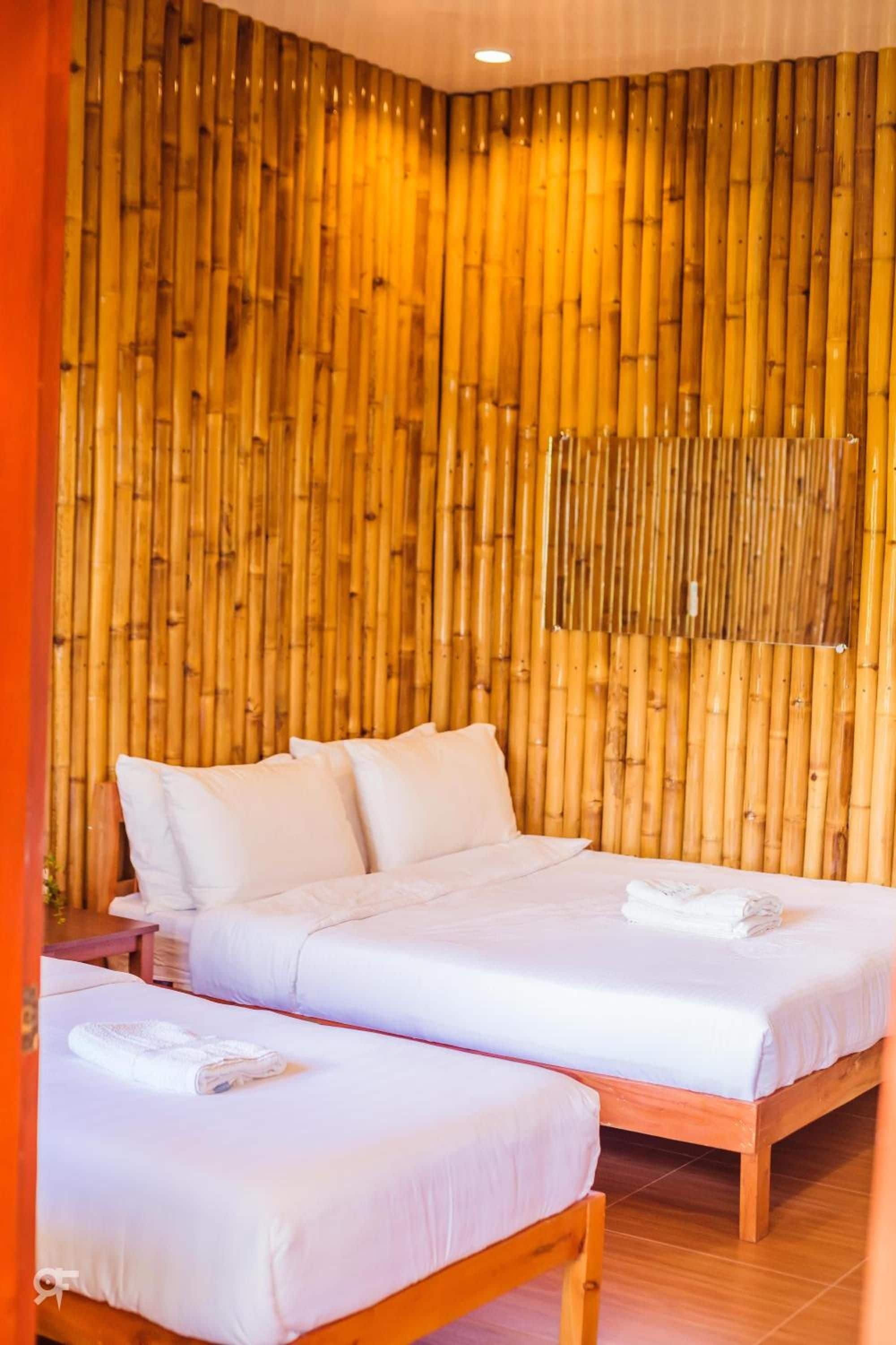 A room with two beds, a wooden floor, and a bamboo wall.