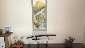A room with a tatami mat floor, a dark wooden table, a small cabinet, and a wall-mounted shelf with decorative items. - Kanazawa-Hachitabi Sennichi (Kanazawa)