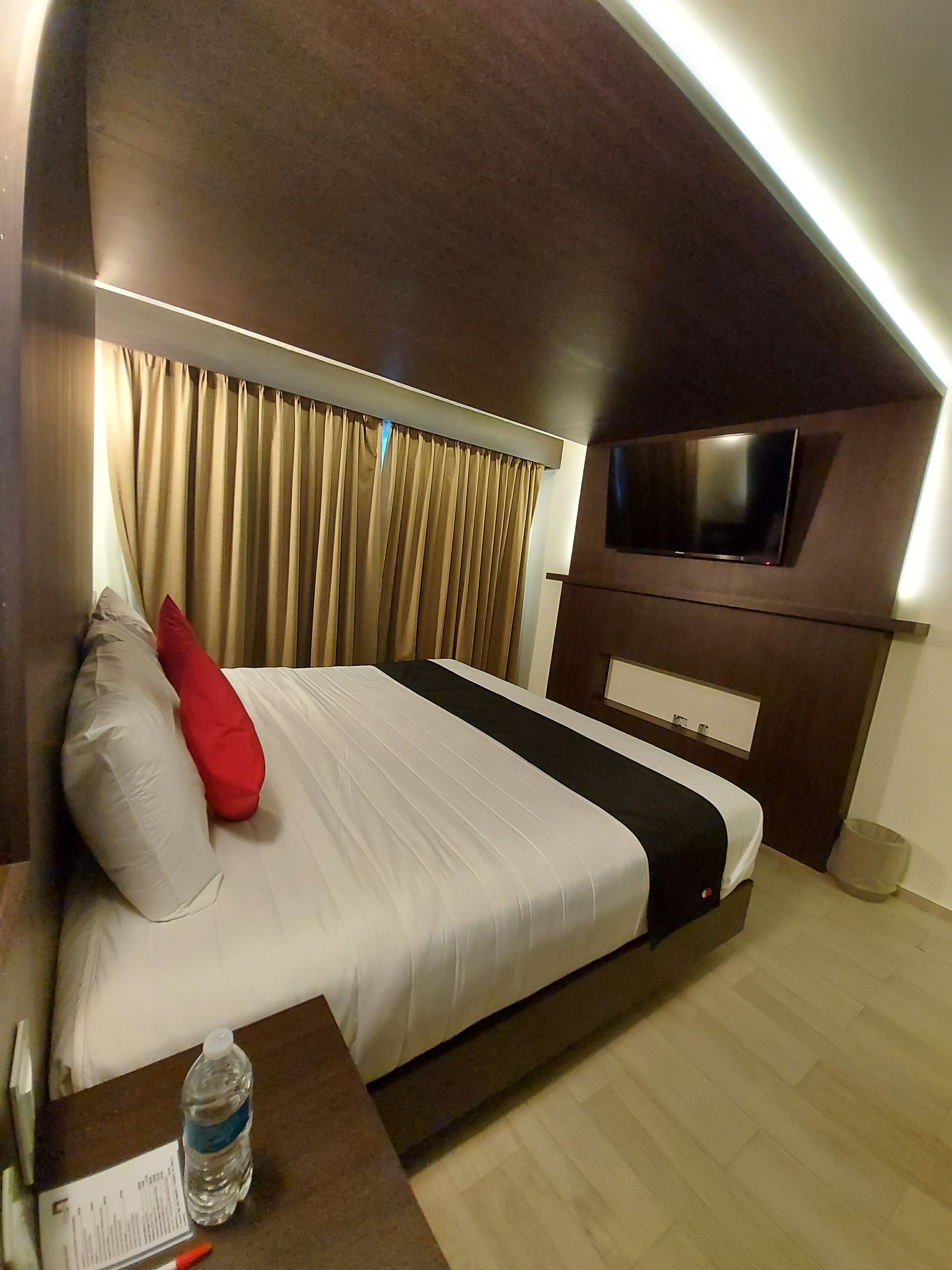 Une chambre d’hôtel avec un lit, un téléviseur fixé au mur, une bouteille d’eau et un bloc-notes sur la table de chevet.