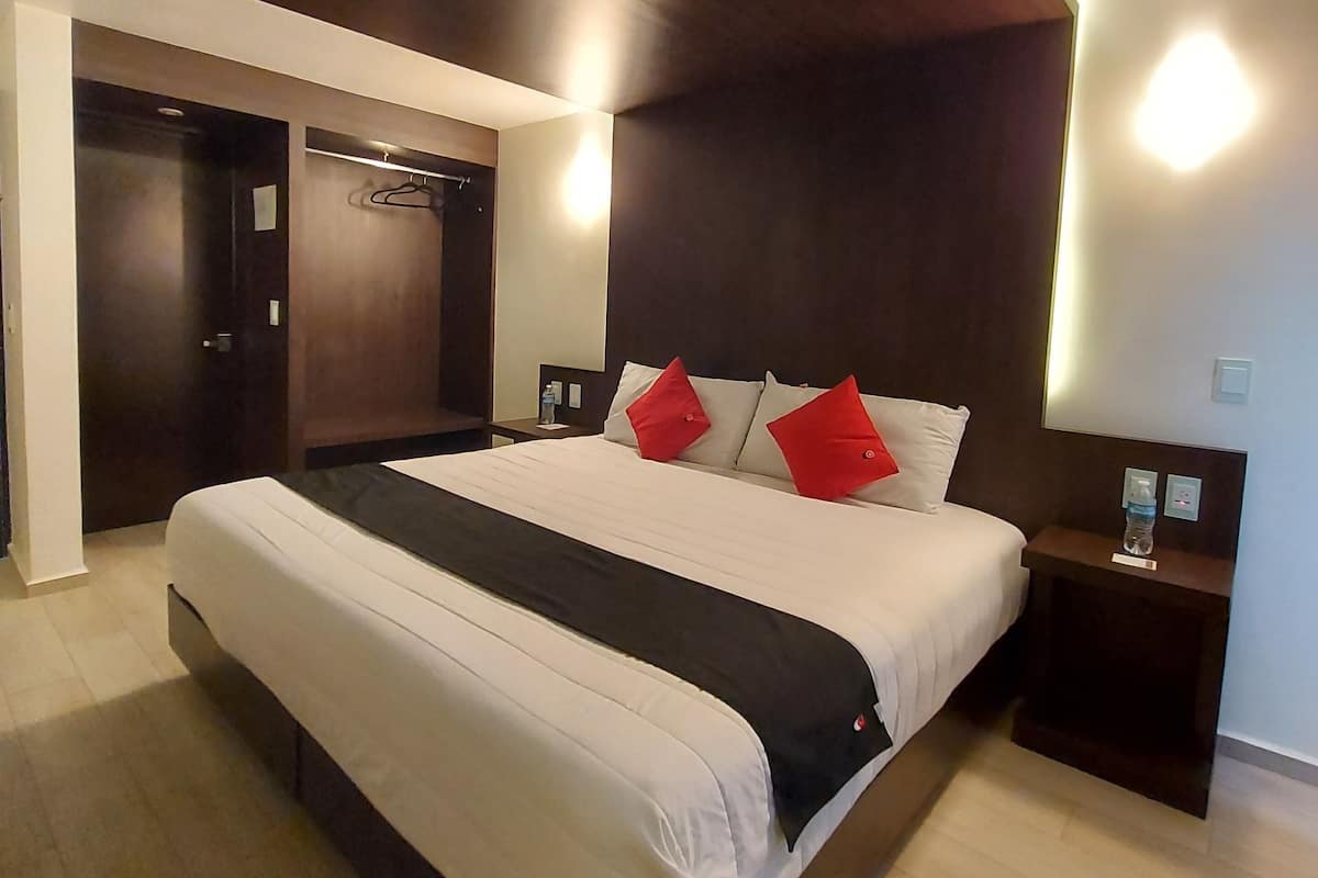 Een moderne slaapkamer met een groot bed, een donker houten hoofdbord en een klein nachtkastje met een waterfles.