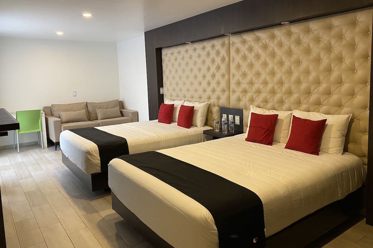 Een hotelkamer met twee bedden, een bank, een klein tafeltje en een groene stoel.