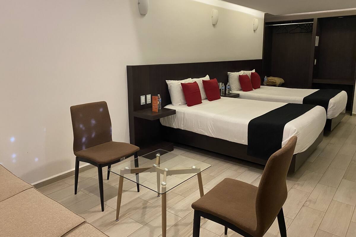 Een hotelkamer met twee bedden, een stoel, een klein tafeltje en een garderobe.
