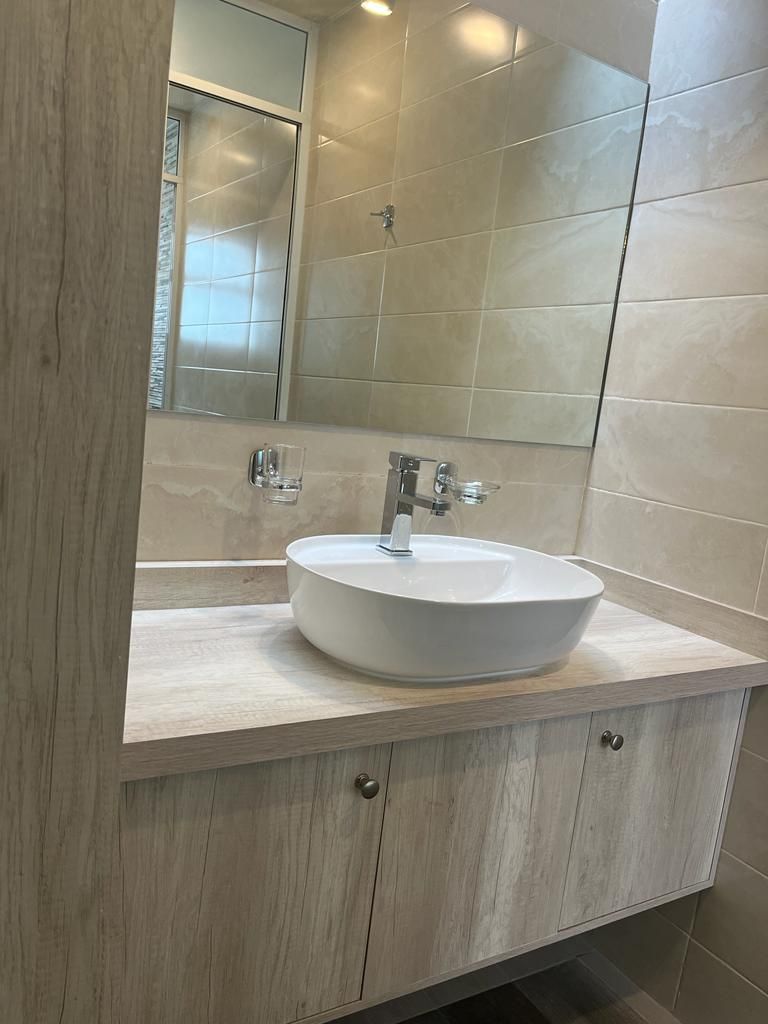 A modern bathroom with a round white sink, a mirror above it, and light-colored wooden cabinetry.